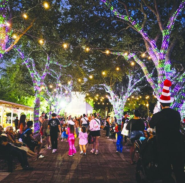 Crowds walking under light-wrapped trees at the Halloween midway