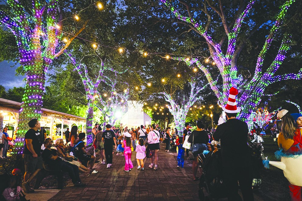 Crowds walking under light-wrapped trees at the Halloween midway