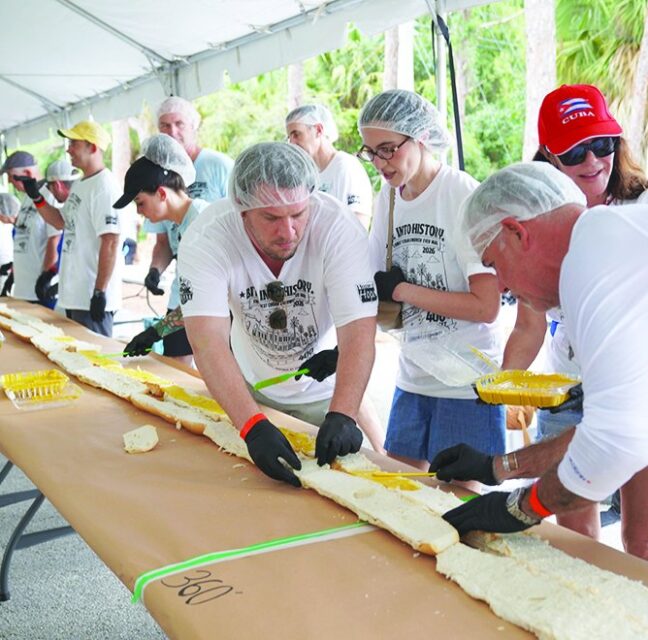 Volunteers in hairnets assembling a 400-foot Cuban sandwich under a tent