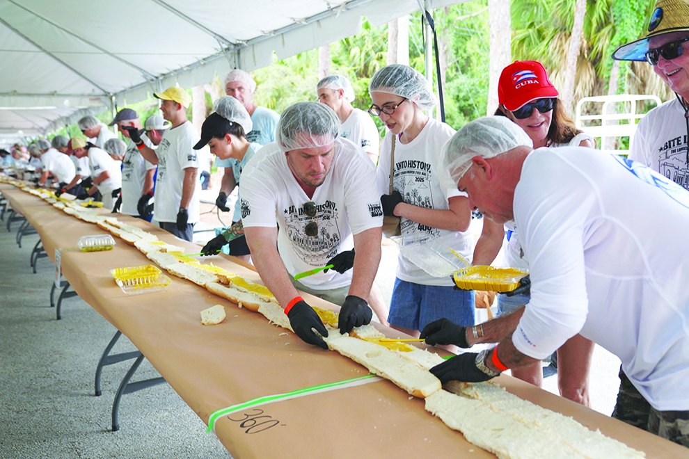 Volunteers in hairnets assembling a 400-foot Cuban sandwich under a tent
